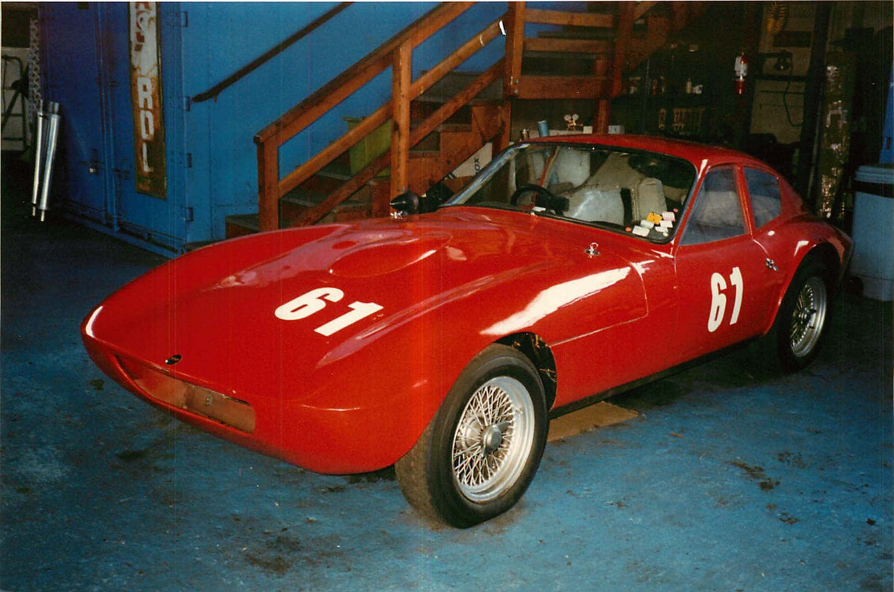 A low red Morgan racing coupé, race number 61, on wire wheels inside a workshop