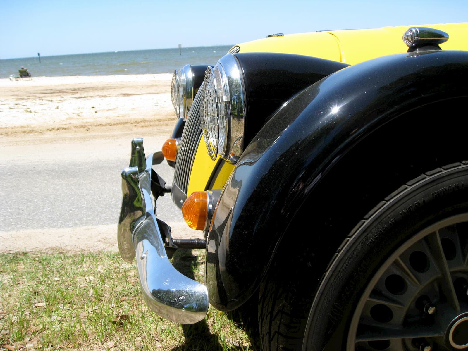 The yellow and black Plus 8 photographed head-on beside a beach