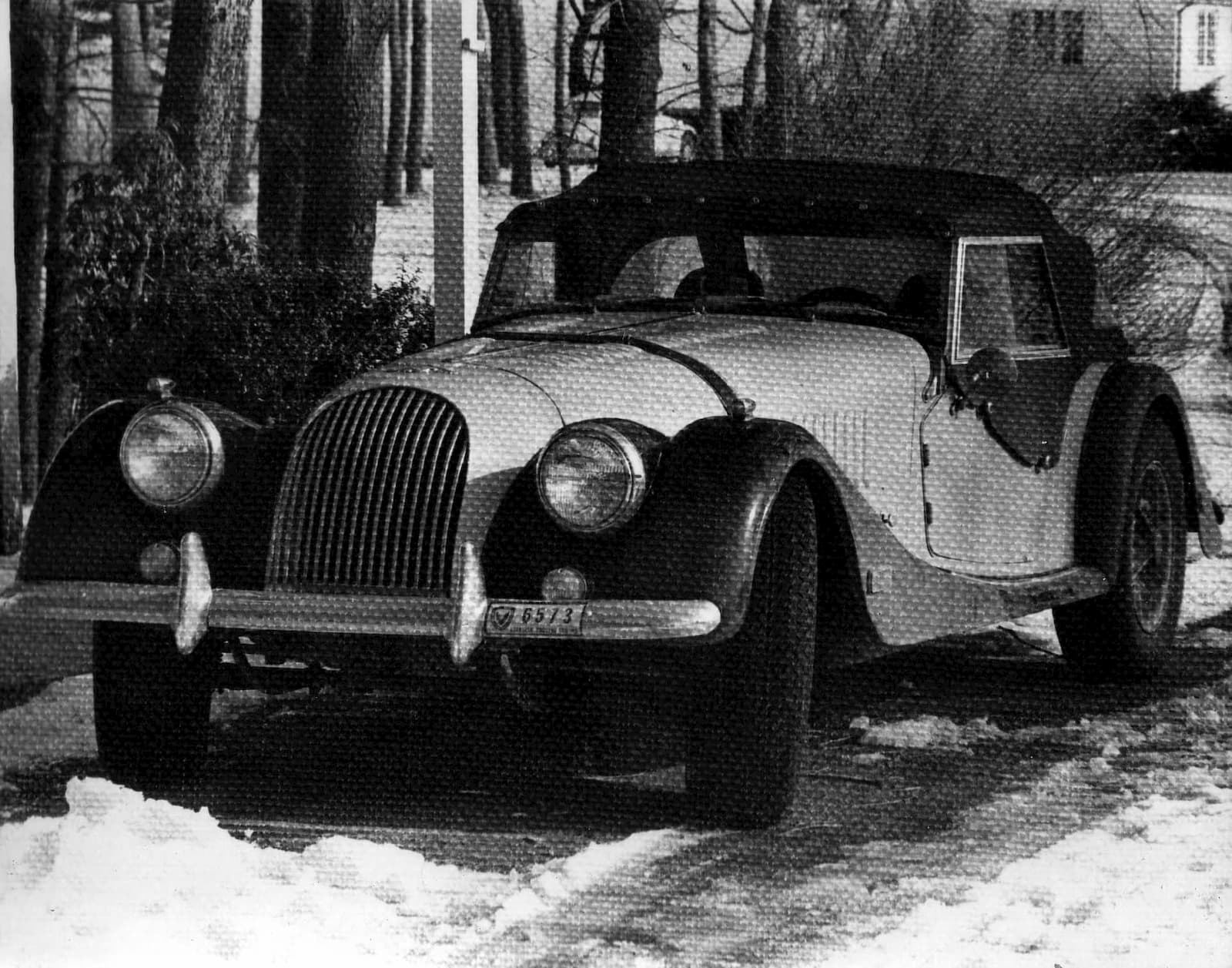 A black-and-white photograph of the Morgan, top up, on a snow-edged driveway